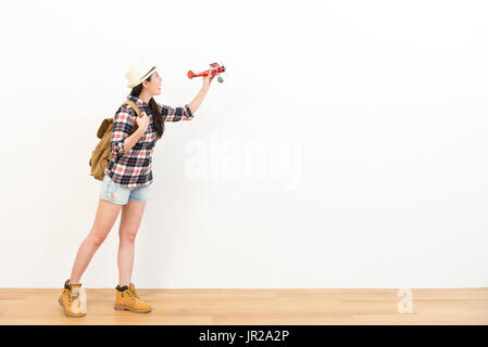 sweet young student traveler playing vintage airplane model toy standing on wooden floor with white wall background. Stock Photo