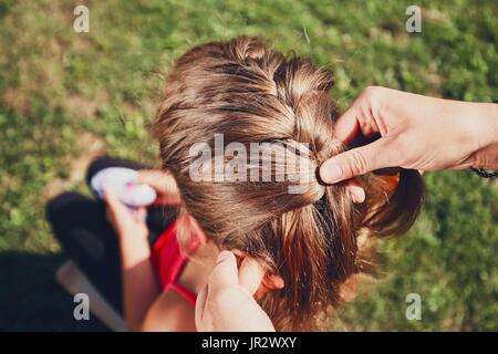Young woman making hair braids of the little girl on the garden in the countryside. Stock Photo