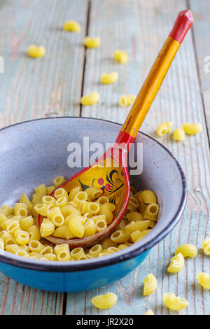 dry pasta on a wooden table in an iron bowl with a wooden spoon Stock Photo
