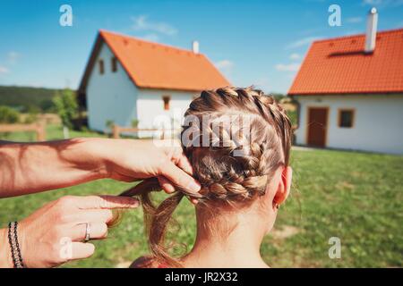 Young woman making hair braids of the little girl on the garden in the countryside. Stock Photo