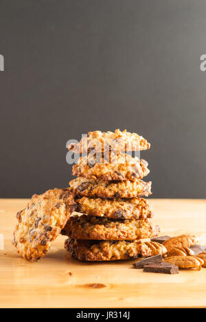 Stacked chocolate chip cookies, white bowl with cookies, pecan and pieces of chocolate on a black background Stock Photo