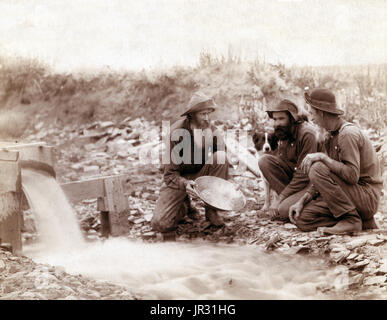 Washing and panning gold, Rockerville, Dakota. Old timers, Spriggs, Lamb and Dillon at work. The Black Hills Gold Rush began in 1874. The first arrivals were a force of one thousand men led by George Armstrong Custer to investigate reports that the area contained gold, even though the land was owned by the Sioux. They found small amounts of gold in present day Custer, South Dakota, and looked for better paying locations. They moved north, establishing the towns of Hill City, Sheridan, and Pactola. At each spot they found flakes of gold, but not the bonanza they sought. Things changed when the  Stock Photo