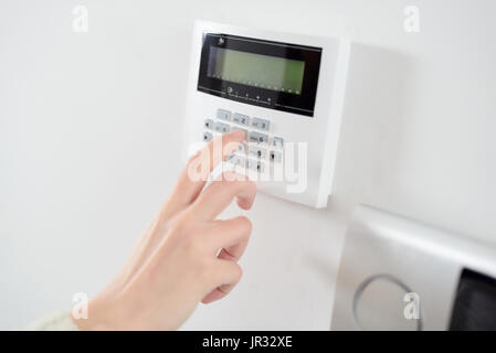 Close up on brunette woman's hand entering code on keypad of home security alarm. Video intercom next to alarm keypad. Stock Photo