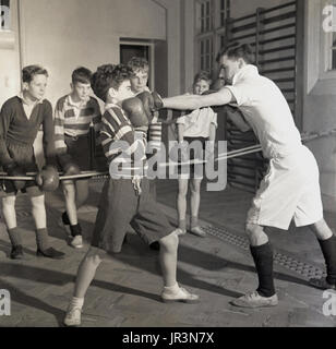 1948, England, a young school boy being taught defence in the sport of boxing by a male sports teacher, while other boys look on and learn, Hailleybury Public School, a traditional British boy's only boarding school. Stock Photo