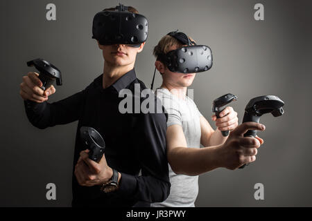 Cheerful friends are watching modern headset at grey background Stock Photo