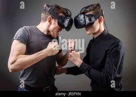two guys wearing in virtual reality glasses stand face to face and want to fight Stock Photo