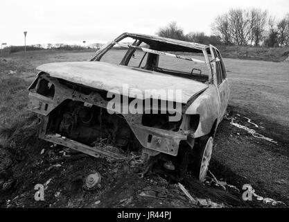 Burnt out abandoned motor car on the side of an isolated road. Stock Photo