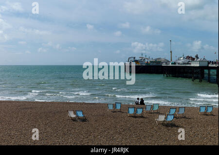 couple sitting on Brighton beach amid empty deckchairs Stock Photo