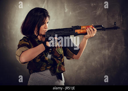 Attractive girl standing in the attitude of aiming and looking through the sight automatic rifle. Stock Photo