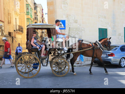 Tourists riding in a horse and carriage on Mediterranean Street, in Valletta, Malta Stock Photo