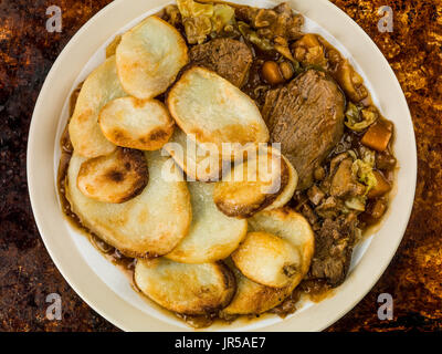 Lamb Hotpot With Sliced Potatoes and Onion Gravy Against a Distressed Burnt Oven or Baking Tray Stock Photo