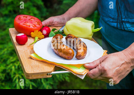 Female hands holding plate with grilled sausages in the garden Stock Photo