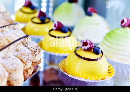 Displays a selection of colourful French pastries and dome-shaped mousse cakes topped with fresh berries, Villepinte, France Stock Photo