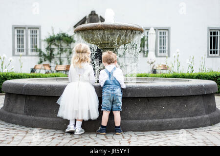 backview Little girl and boy in wedding dress with old classic style stone fountain with flowing water concept sewwt love romantic be togehther couple Stock Photo