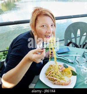 Middle-aged Caucasian woman eating seafood pasta in italian restaurant. Stock Photo