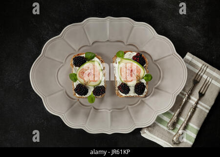 Plate with toasts made by wholemeal bread, cream cheese, blackberries and figs, flat lay. Stock Photo