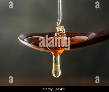 Honey pouring on wooden spoon and dripping from spoon. Dark background. Extreme close up. Stock Photo