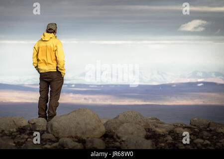 Man standing on mountain, looking relaxed towards snowy mountain range. Stock Photo