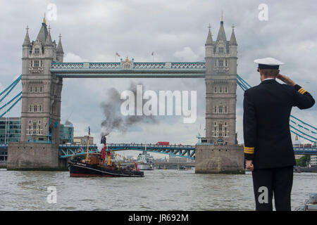 The ST Portwey, a 90-year-old steam tug, which was built on the Clyde in 1927, and which came under command of the Royal Navy during the Second World War, is saluted by Commander Richard Pethybridge as she steams past HMS President, the Royal Navy's permanent shore establishment on the River Thames in London, as they mark the tugs 90th birthday. Stock Photo
