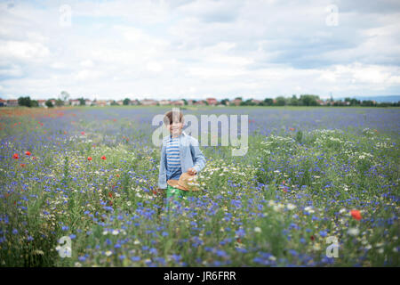 Smiling boy walking through a wildflower meadow carrying his hat Stock Photo