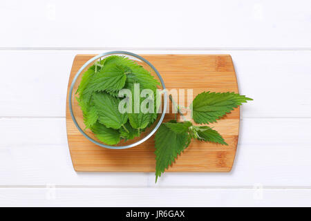 bowl of fresh nettle leaves on wooden cutting board Stock Photo