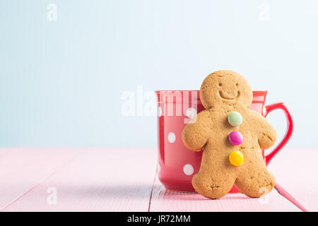 Gingerbread man leaning against a cup on pink table. Xmas gingerbread. Stock Photo