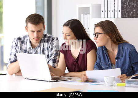 Three entrepreneurs coworking on line with a laptop sitting in a desktop at office Stock Photo