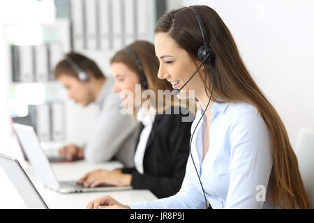 Side view of a telemarketer working on line at office with other workers in the background Stock Photo