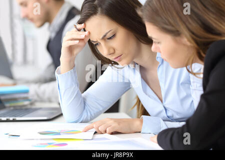 Two worried businesswomen analyzing paper growth graphs at office Stock Photo