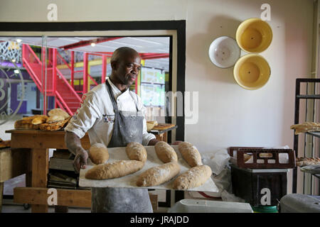 African baker carrying tray of loaves of bread in bakery Stock Photo