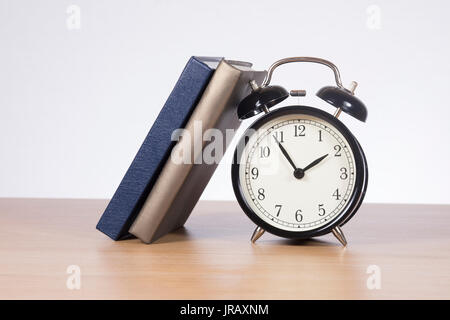 Two books leaning against alarm clock standing on wooden desk Stock Photo