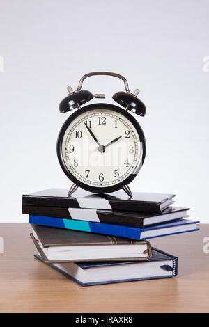 Alarm clock standing on pile of notebooks against plain background Stock Photo