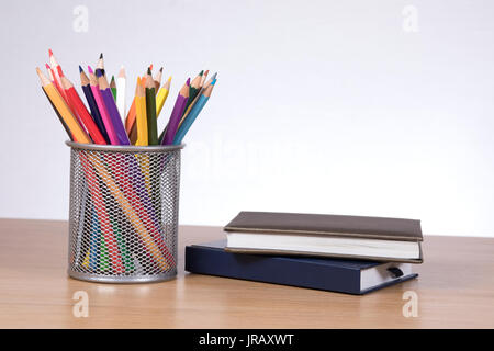 Colore pencils in container standing by two notebooks on desk against plain background Stock Photo