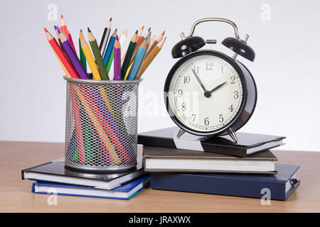 Alarm clock, colored pencils in holder standing on pile of notebooks Stock Photo