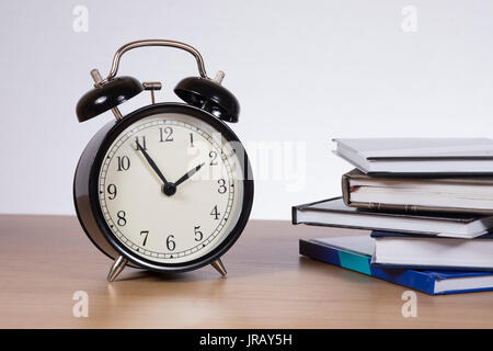 Alarm clock standing on table by stack of books against plain background Stock Photo