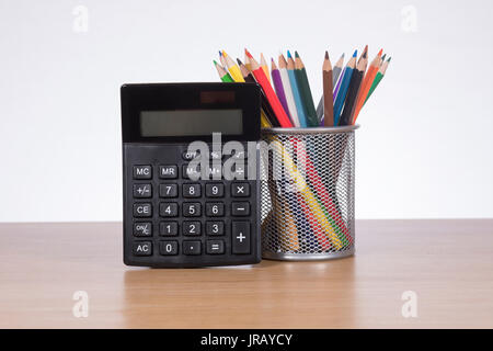 Calculator with colored pencils in container standing on desk Stock Photo