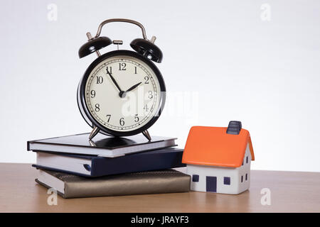 Alarm clock standing on pile of books by miniature of house Stock Photo