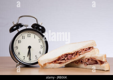 Alarm clock standing by sandwich with meat on table Stock Photo