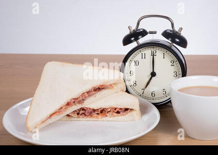 Alarm clock standing between meat sandwich served on plate with cup of coffeep of coffee Stock Photo