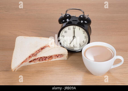 High angle view of alarm clock standing between meat sandwich cut in half served on plate and cup of coffee Stock Photo