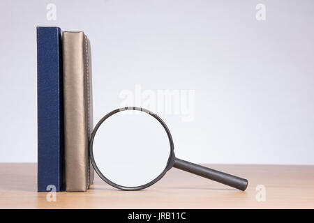 Magnifying glass with a business diary and journal standing upright on a wooden desk with large copy space on a blank white wall behind Stock Photo