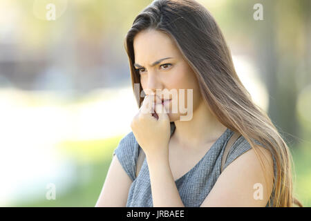 Nervous woman biting nails and looking away alone outdoors in the street Stock Photo