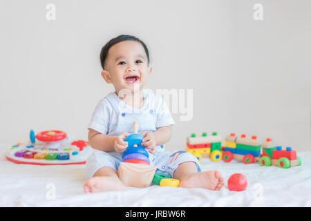 Adorable Asian baby boy 9 months sitting on bed and playing with color developmental toys at home. Stock Photo