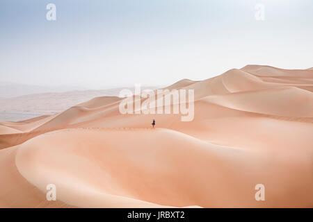 woman running down a dune in Rub al Khali Desert at the Empty Quarter, in Abu Dhabi, United Arab Emirates Stock Photo