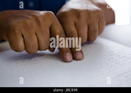Cropped fingers on senior man reading braille book at table in nursing home Stock Photo