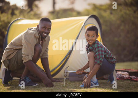 Portrait of smiling father and son pitching their tent in park on a sunny day Stock Photo