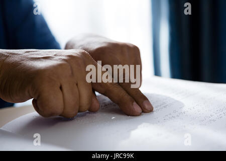 Cropped hands on senior man reading braille book at table in retirement home Stock Photo