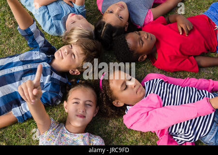 Overhead view of children with arms raised lying on field in yard Stock Photo