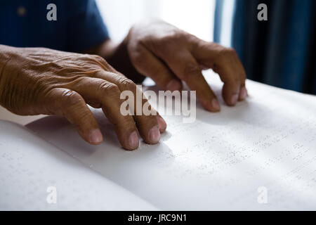 Cropped hands on retired man reading braille book at table in retirement home Stock Photo