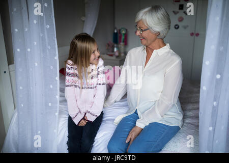 Smiling grandmother and granddaughter interacting with each other on bed in bedroom Stock Photo